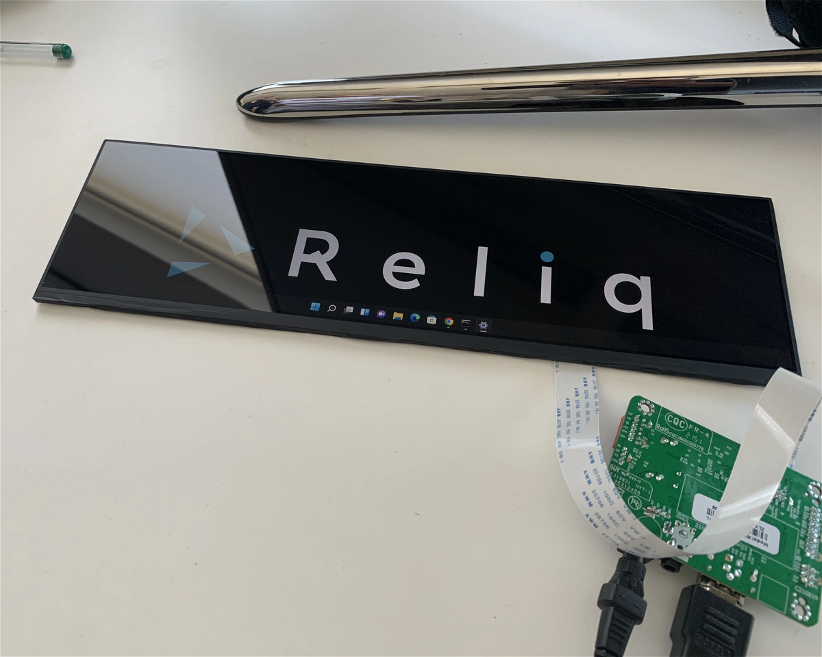 A 1920 by 515 sample panel on the desk, lit up and showing the Reliq logo