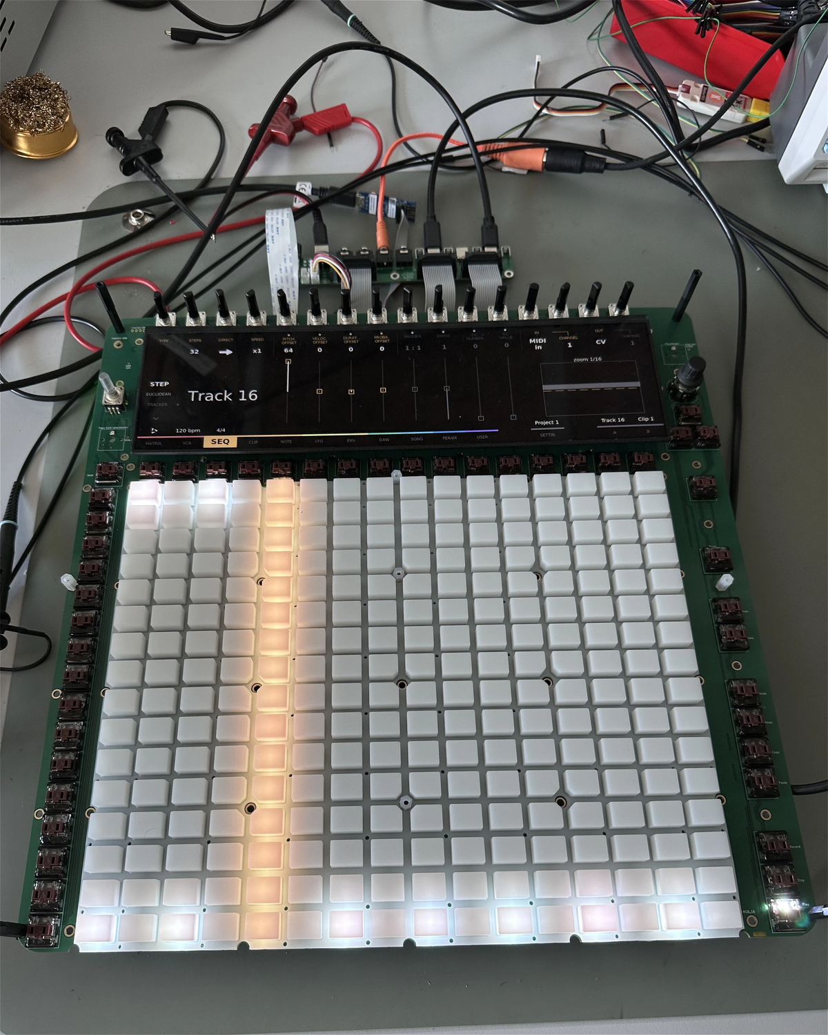 Reliq prototype with sixteen encoders above the screen and the pad grid below, on a workbench
