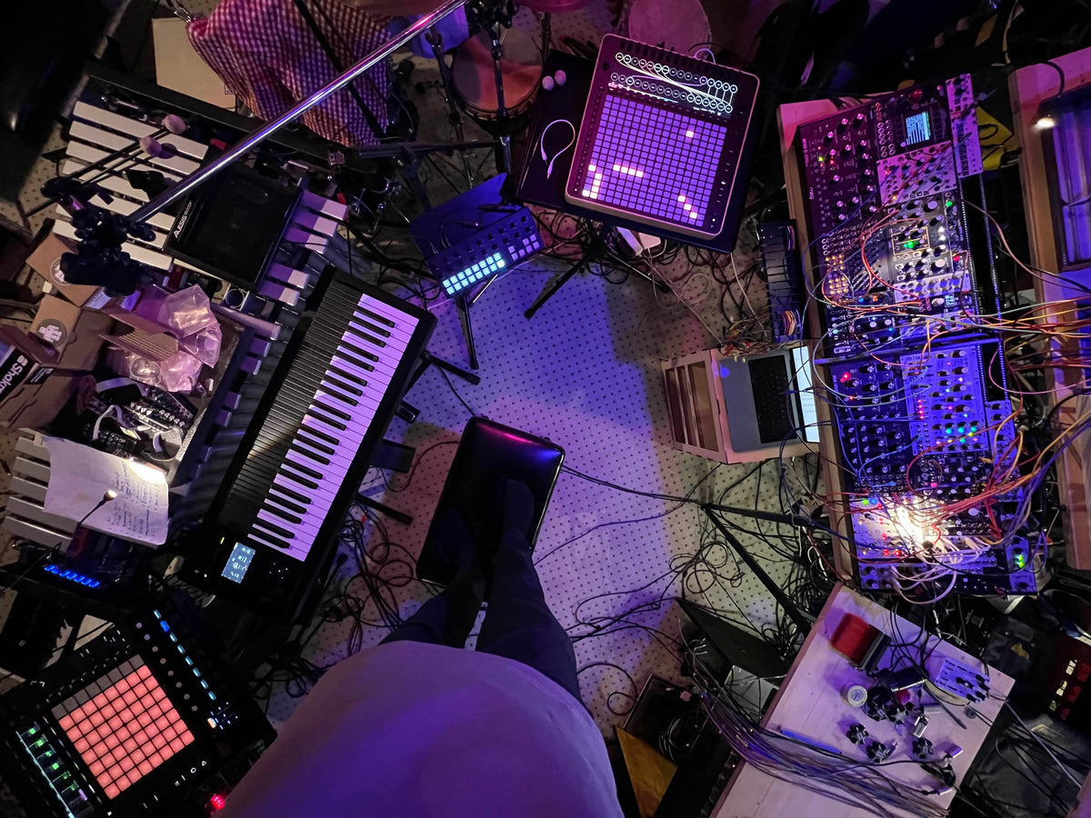 Reliq at the centre of a studio of synths, a modular rig and a keyboard, seen from above