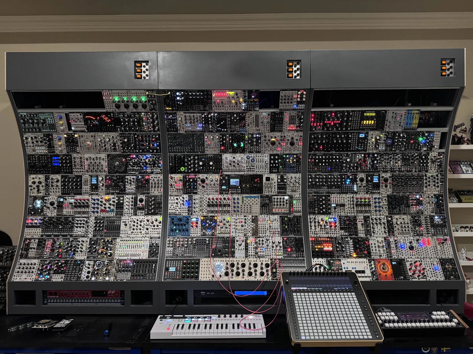 A wall of Eurorack modules with Reliq on the desk in front of it