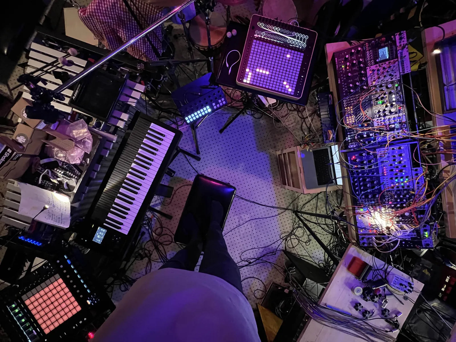 A live setup seen from above, with Reliq on a stand among keyboards and modules